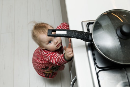 child safety at home concept – toddler reaching for pan on the s