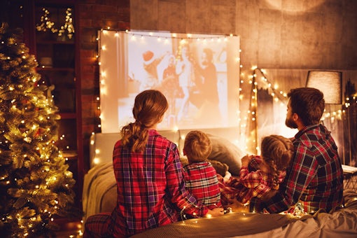 family mother father and children watching projector, film, movies with popcorn in   christmas evening   at home