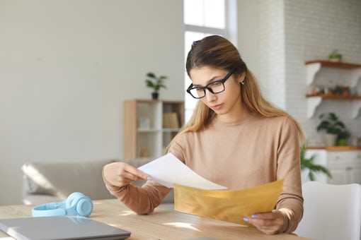 Anxious young woman at home taking letter from envelope reads bad negative news.