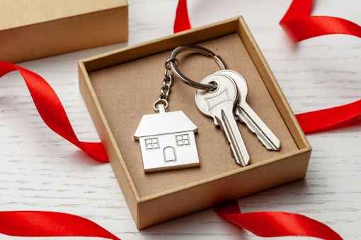 Keychain house and keys with red ribbon and gift box on white wooden background