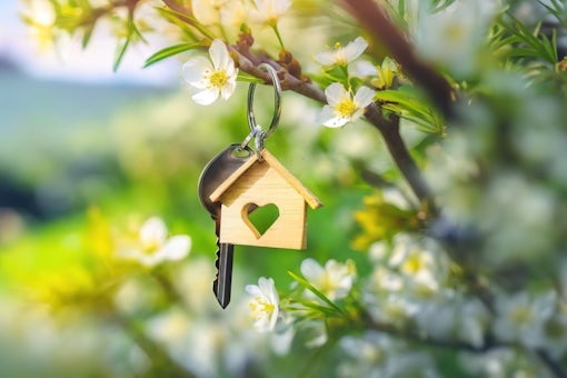 On a branch speckled with flowers, a key dangles, hinting at the joys of homeownership and new starts. A key ring with a house shape hangs on a blooming branch, embodying home dreams.