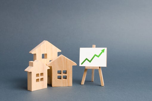 Wooden figures of houses and a poster with green arrow up. Increase liquidity and attractiveness of assets. Raising the rent or cost of buying a home.The concept of real estate value growth.