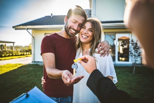 Happy millennial couple receiving keys from realtor, purchasing real estate