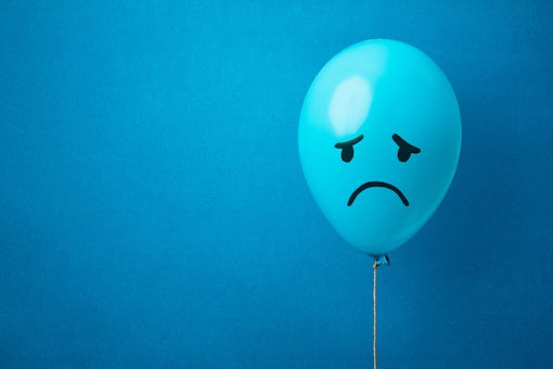 Stock photo of a blue balloon on a blue background with a sad face drawn. Blue monday concept