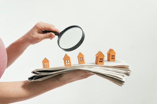 woman holding newspaper using magnifying glass to house hunt