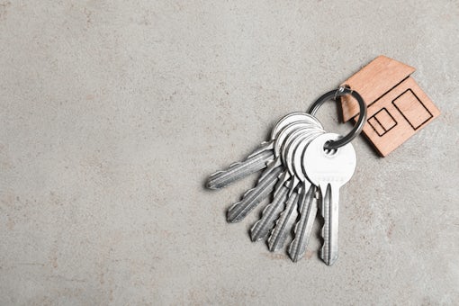 Keys with trinket in shape of house on grey stone background, top view and space for text.