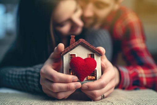 Couple in love hugging and holding a miniature house with a red heart in their hands. House of lovers. Affordable housing for young families. Accommodation for lovers of couples. Valentine's day house