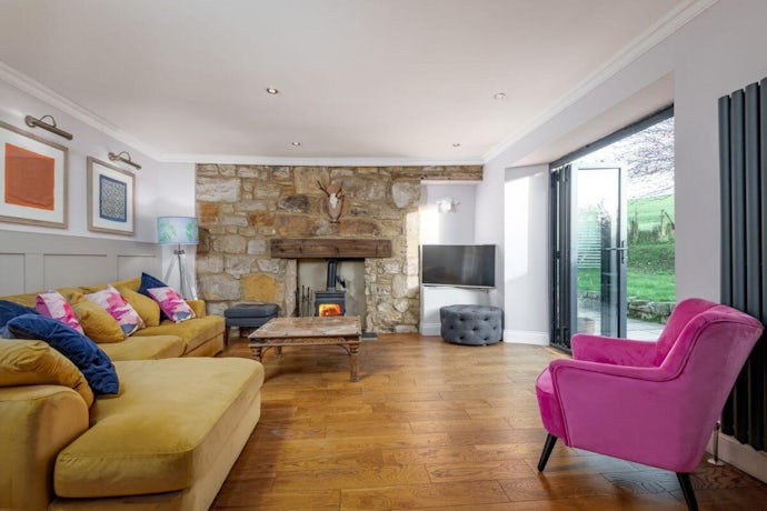 inside the living room of one of our property refurbishments, wooden flooring, pink chair, yellow sofa, glass patio door and fire place