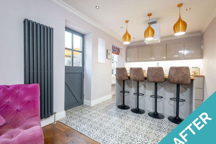 a photo of our east cottage property let after making holiday home improvements open plan kitchen with gold lights, a bar with stools, and pink chair