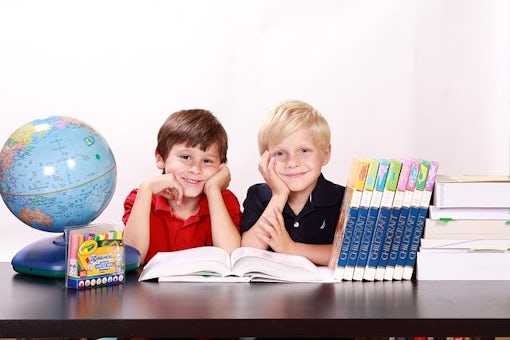 Two children in front of a desk with school supplies.