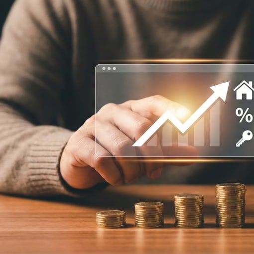 Professional Adult Asian Man Planning Real Estate Investment with Stacks of Coins and Rising Growth Chart Icons Holding House Keys with Sale Sign in Home Office at Night