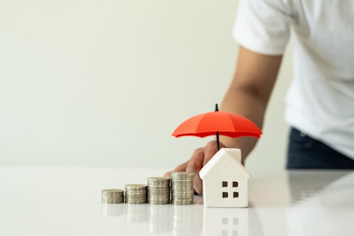 Model house and raised pile with hand holding an umbrella on white background, financial insurance and safe investment concept. Close-up pictures