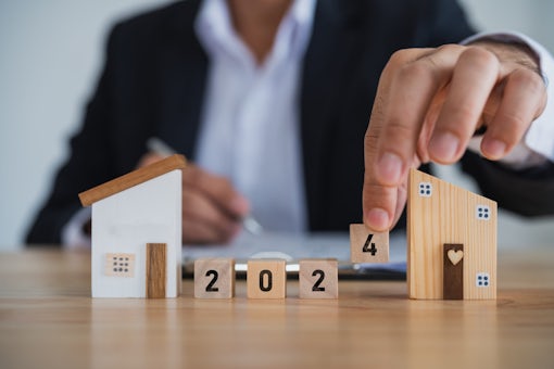 2024 new year target home loan trends. Businessman hold model house and wood blocks word LOAN.