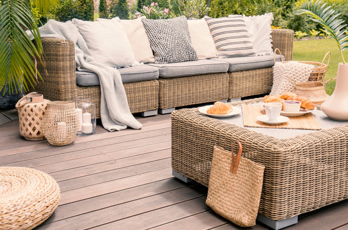 Wicker patio set with beige cushions standing on a wooden board