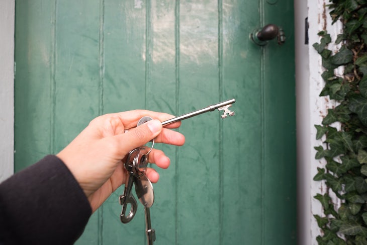 Hand holding old fashioned keys to green door of cottage – home owner, buying or renting concept