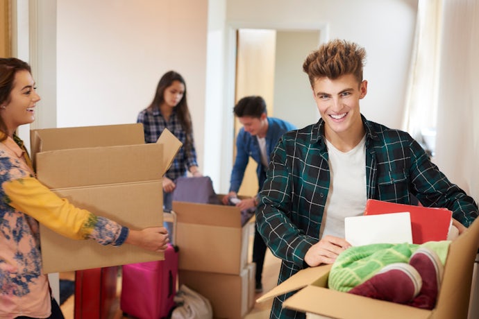Group of young adults smiling while carrying cardboard boxes during a house move in the UK