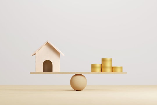 Wooden home and money coins stack on wood scale. Property investment and house mortgage financial real estate concept. 3d illustration