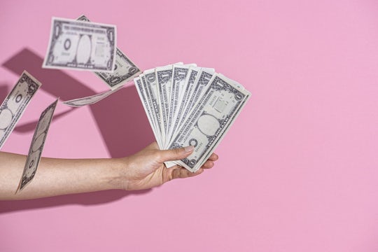 Hand holding cash on a pink wall background