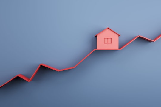 Real estate market and property value increase concept with red house layout on rising red line graph on abstract blue background. 3D rendering