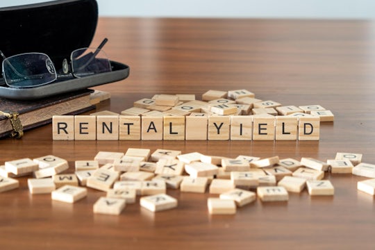 rental yield word or concept represented by wooden letter tiles on a wooden table with glasses and a book