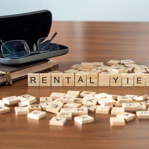 rental yield word or concept represented by wooden letter tiles on a wooden table with glasses and a book
