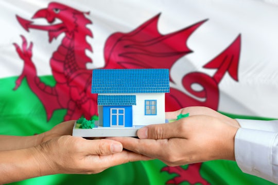 Wales real estate concept. Man and woman holding miniature house in hands. Citizenship theme and national flag on background.